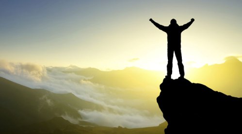 Man standing on cliff with arms in the air